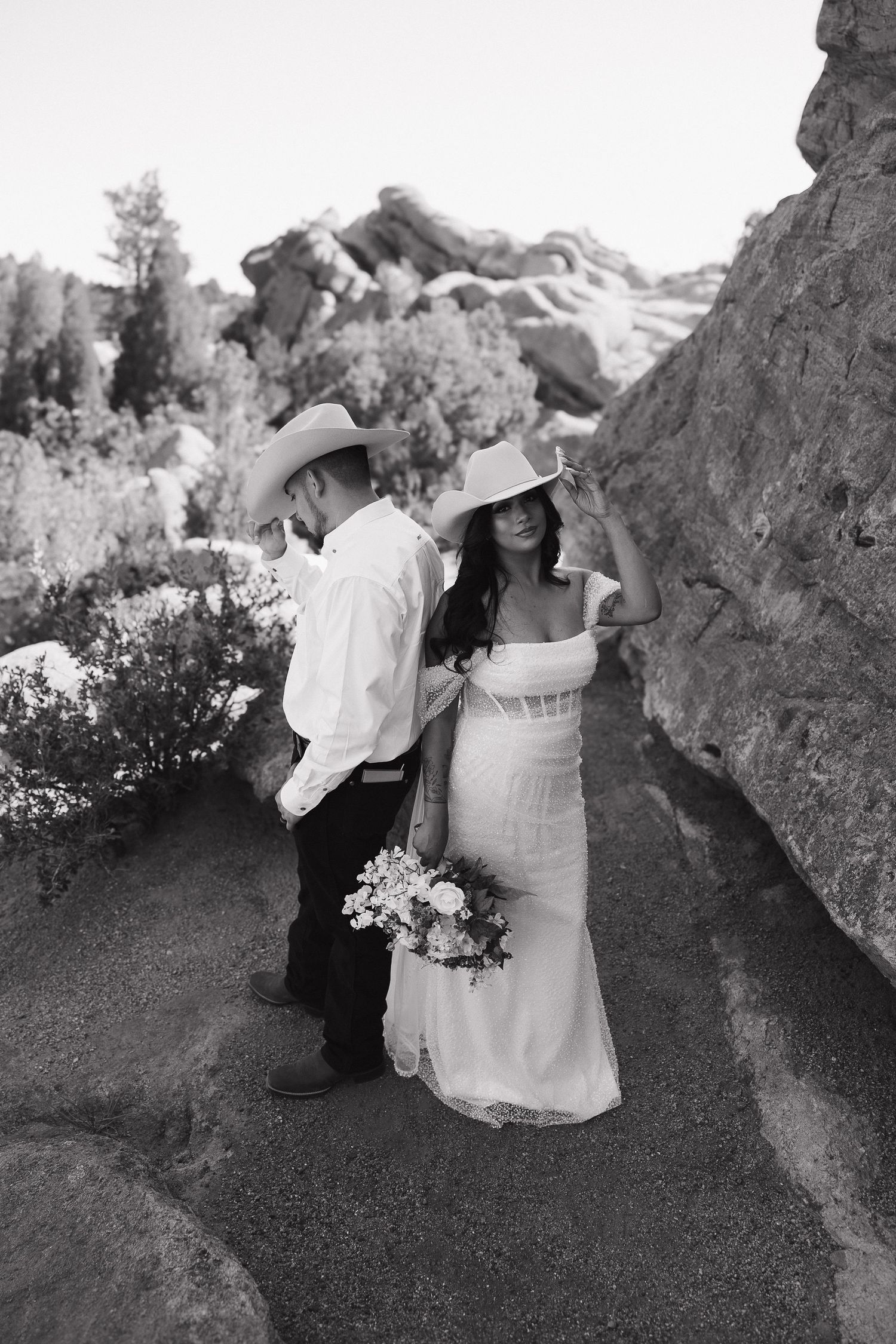 A black and white photo of a romantic wedding couple posing between rock formations in a natural outdoor setting.