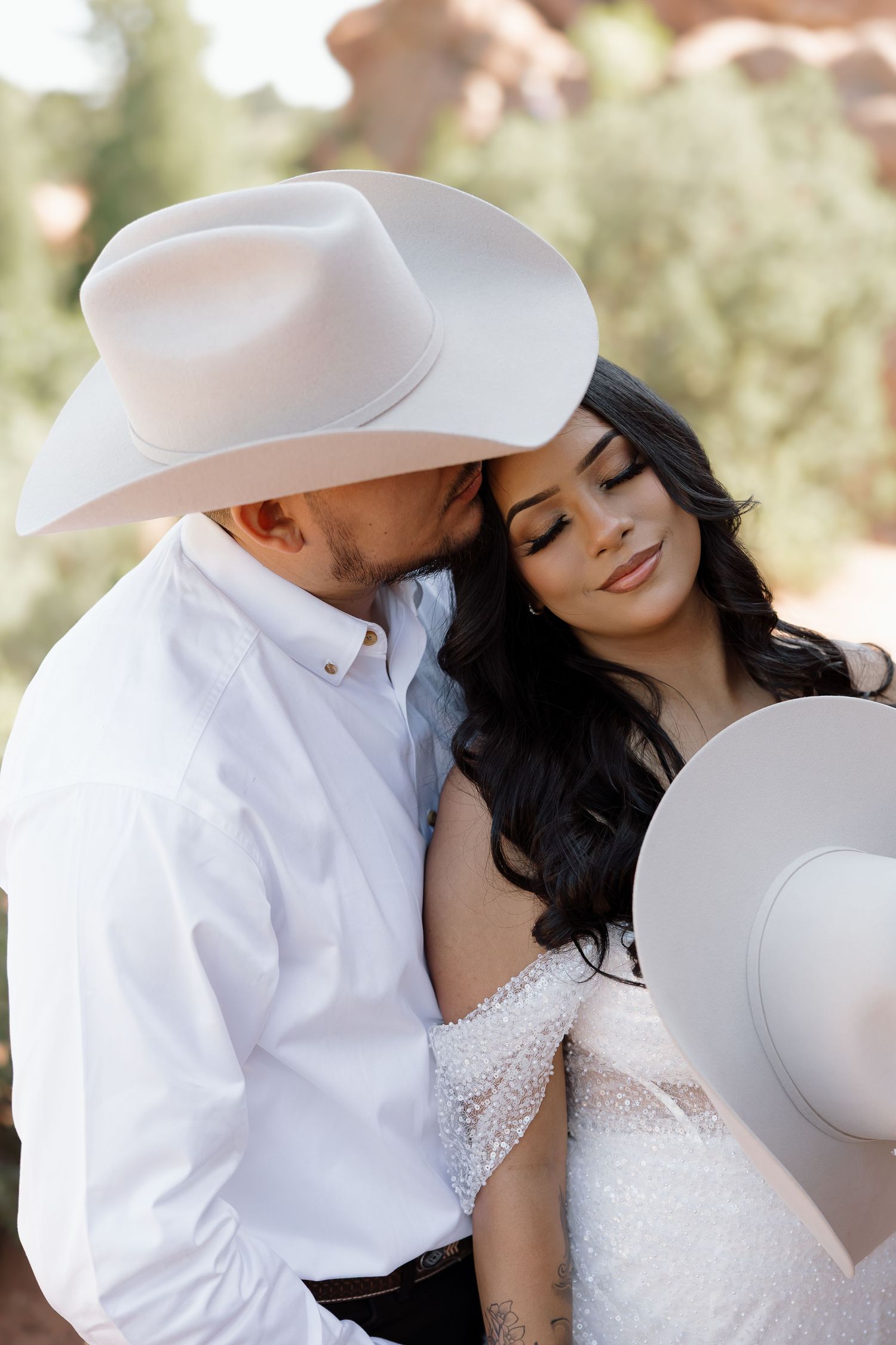 A romantic wedding couple in white cowboy hats share an intimate moment outdoors with soft lighting and natural scenery.