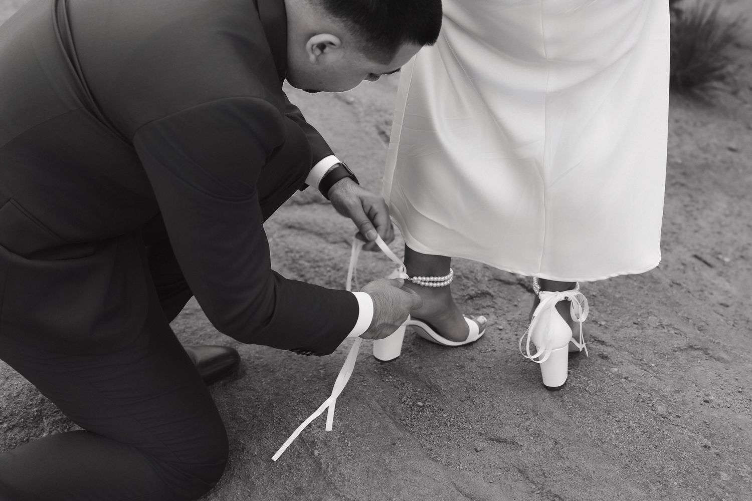 Wedding details showing the tying of white shoelaces and dress buttons against a dark background.