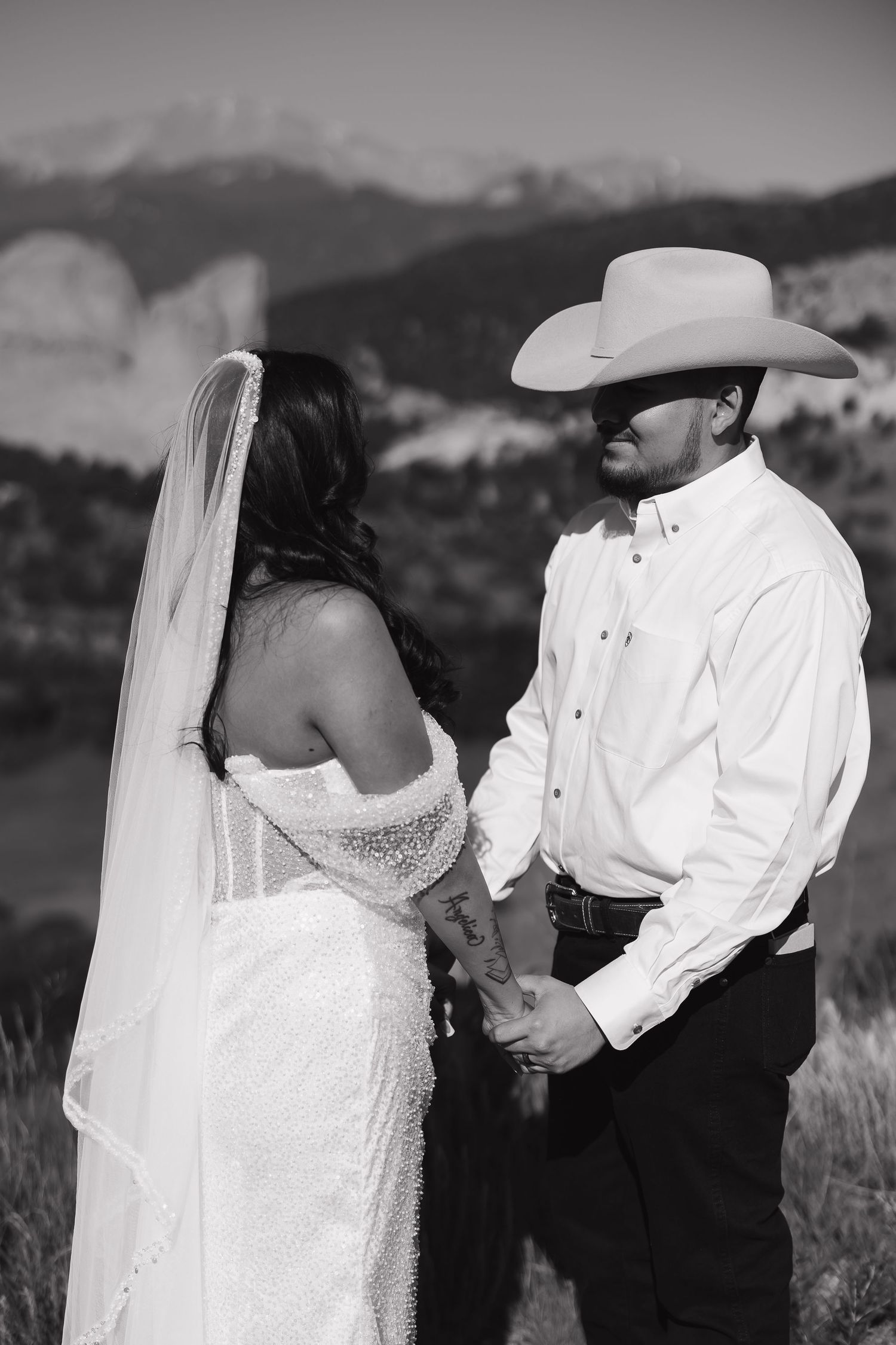 Black and white wedding photo showing a couple in western attire against a mountain backdrop during their ceremony.
