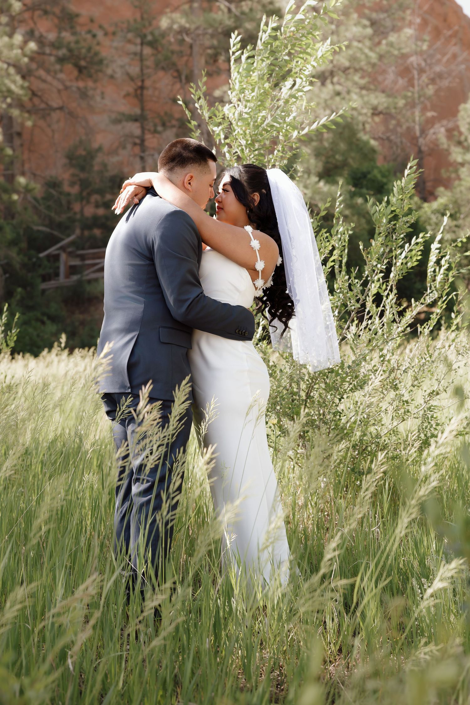 Newlyweds embracing in tall grass with red rock formations in the background.