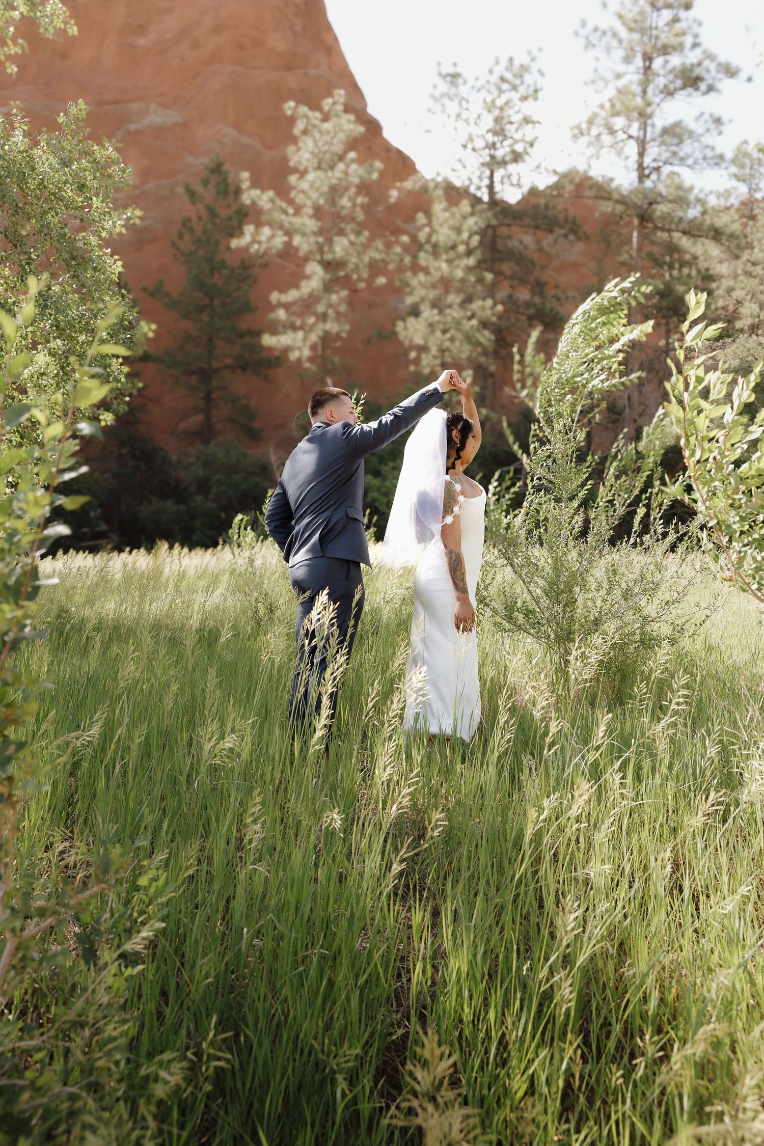 Romantic couple dancing and twirling in a meadow with red rocks and evergreen trees in the background.