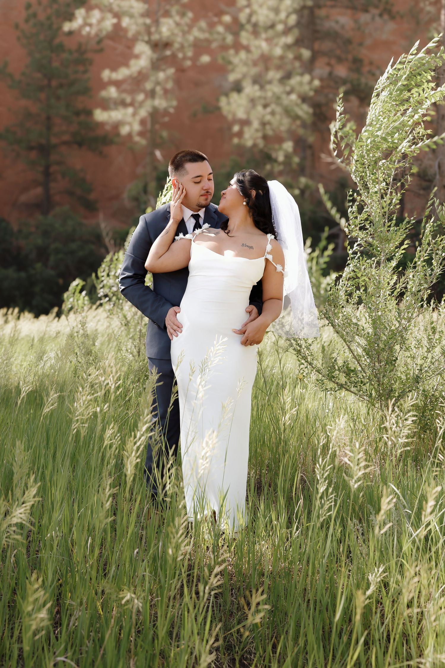 A romantic wedding moment captured in tall grasses with a natural brick wall backdrop.