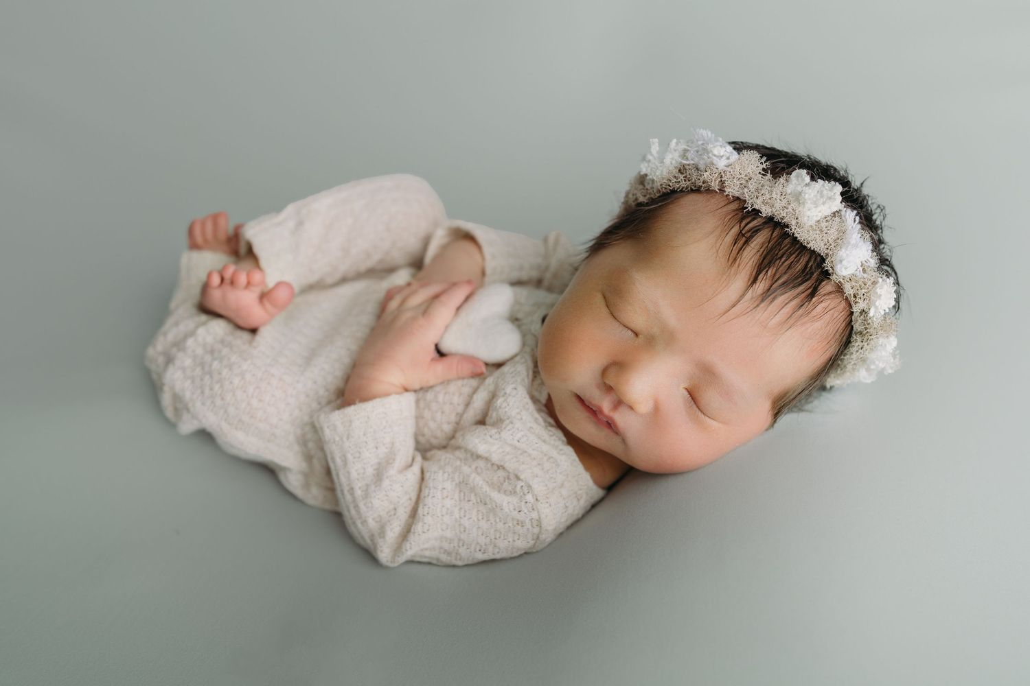 A newborn baby wearing white clothing sleeps peacefully on a soft grey backdrop for newborn photos in Tampa