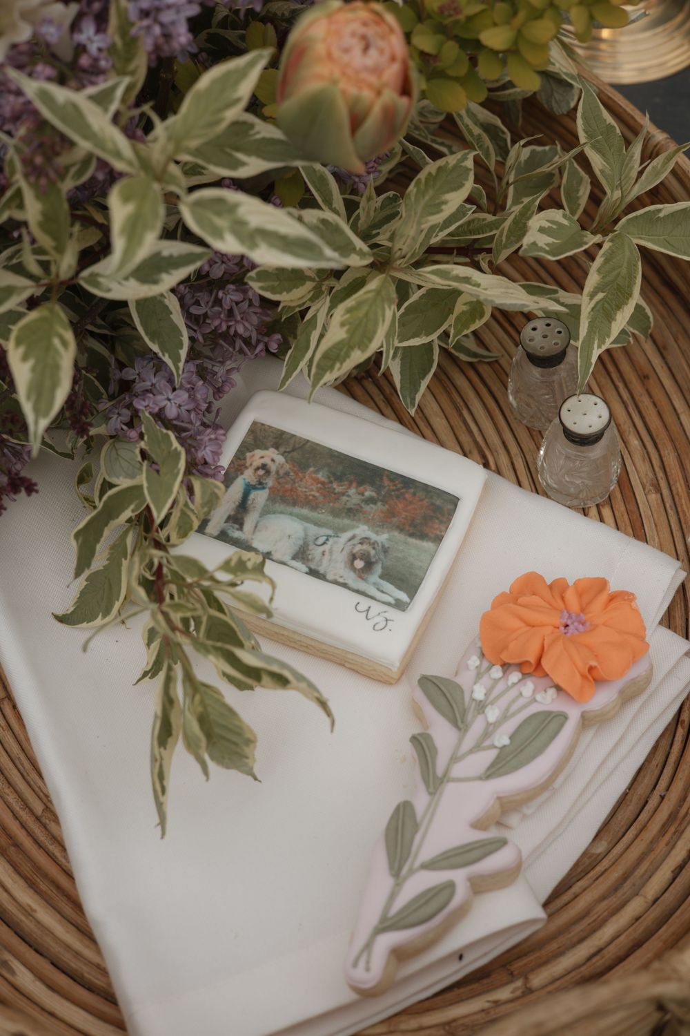 Flatlay with green plants, a polaroid photo, and an orange paper flower on a white surface with wooden accents.