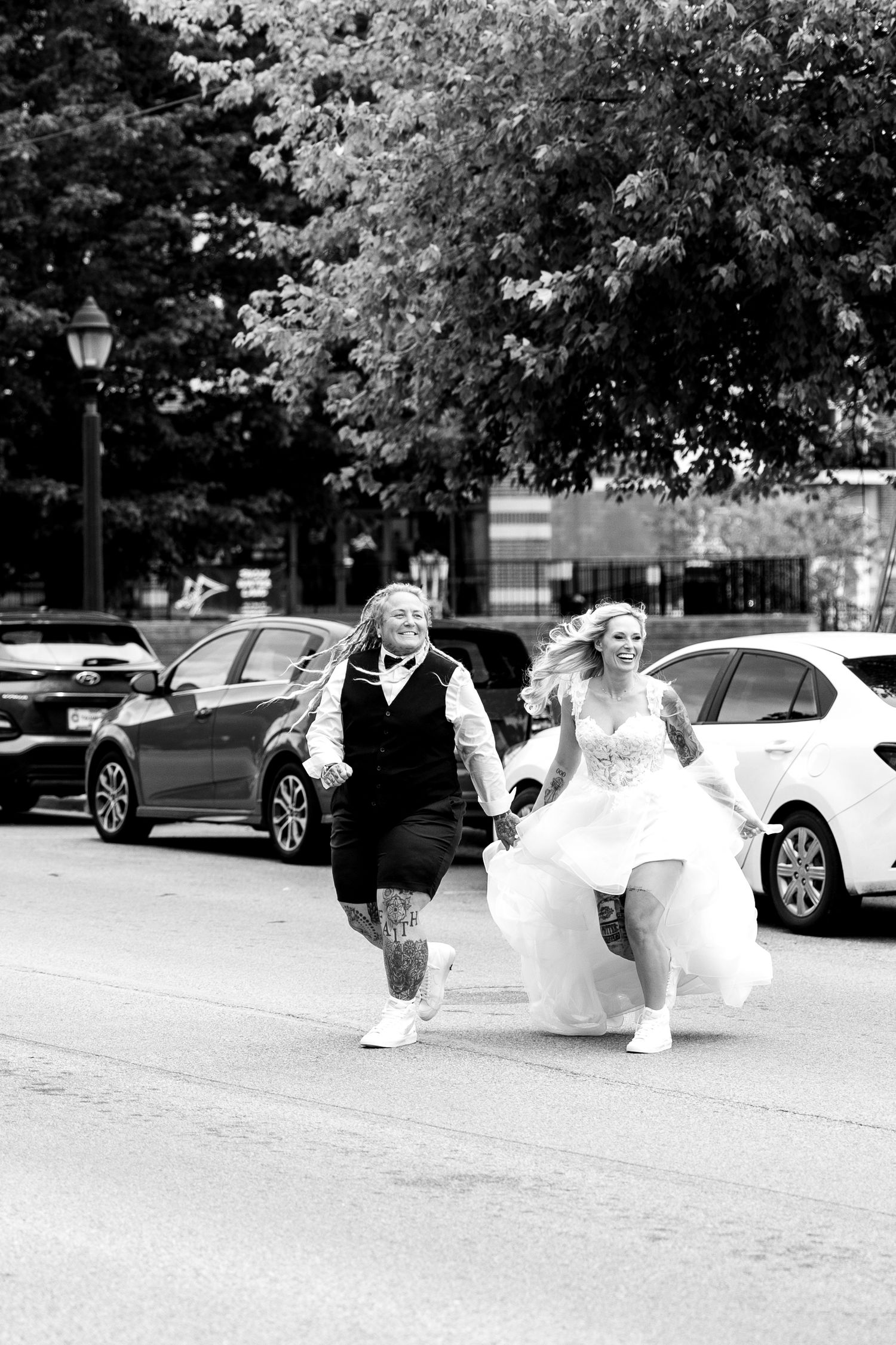 Bride and groom laugh while running across a city street in black and white wedding photo.