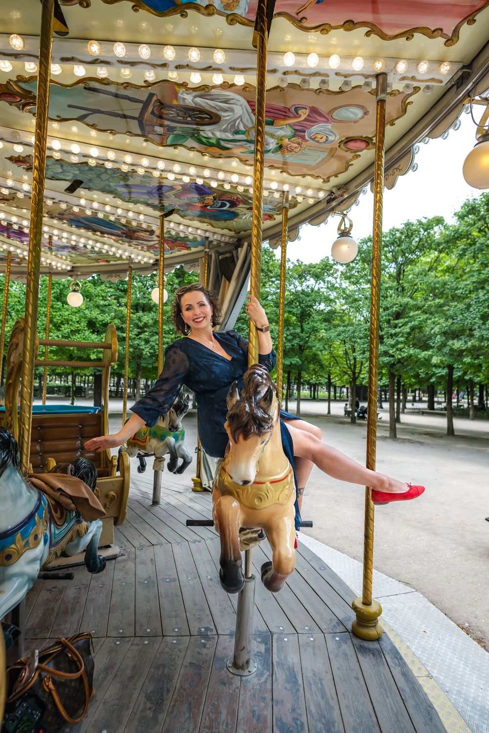 A person rides a decorative carousel animal in a vintage merry-go-round with twinkling lights and painted scenery above.