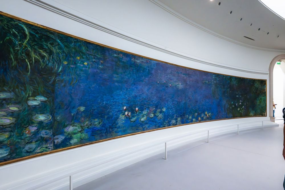 A panoramic view of a long corridor with white walls and ceiling featuring colorful water lillies mural.