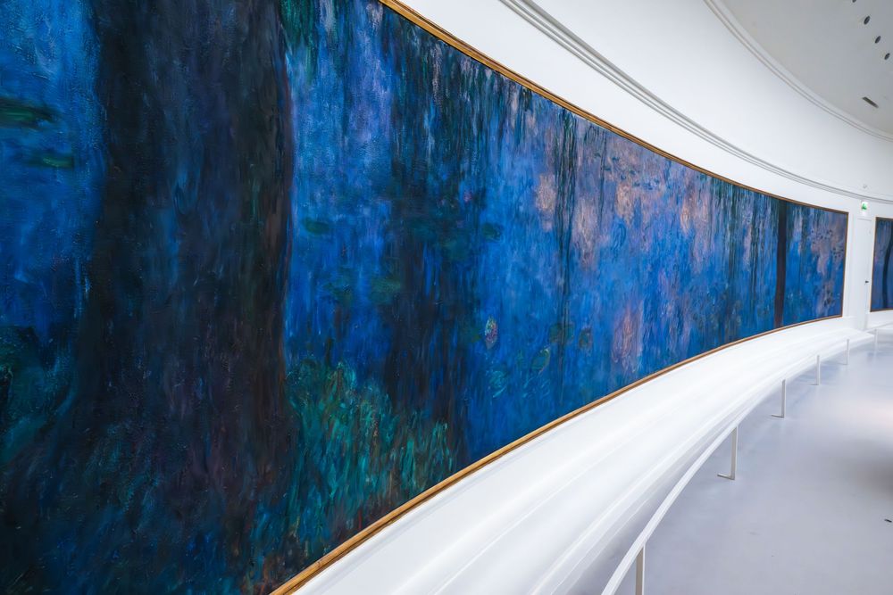 A curved museum hallway features a massive blue Monet water lilies mural along the curved wall.