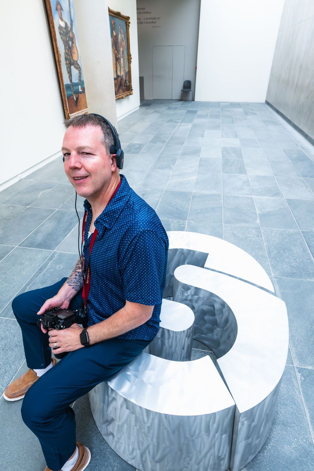 A person sits and poses from different angles on a modern curved white bench in a minimalist gallery space.