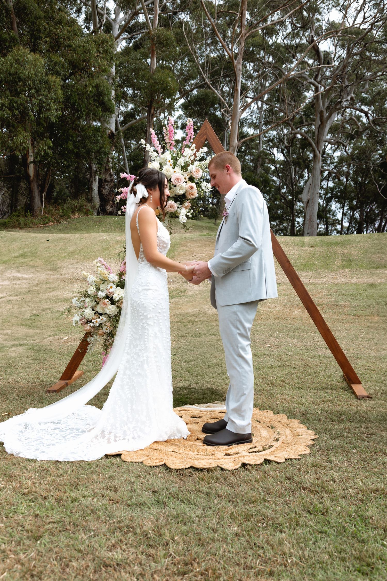 Intimate outdoor wedding ceremony with decorative wooden cross and orange floral arrangements on grassy terrain.