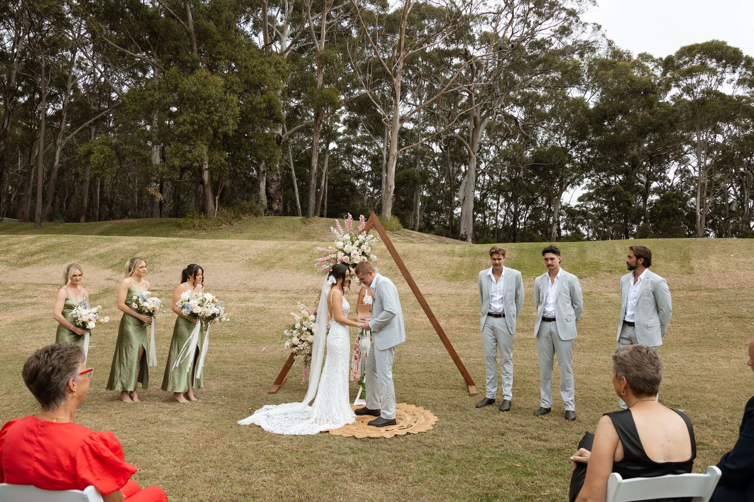 Outdoor wedding ceremony on a grassy hillside with eucalyptus trees in the background.