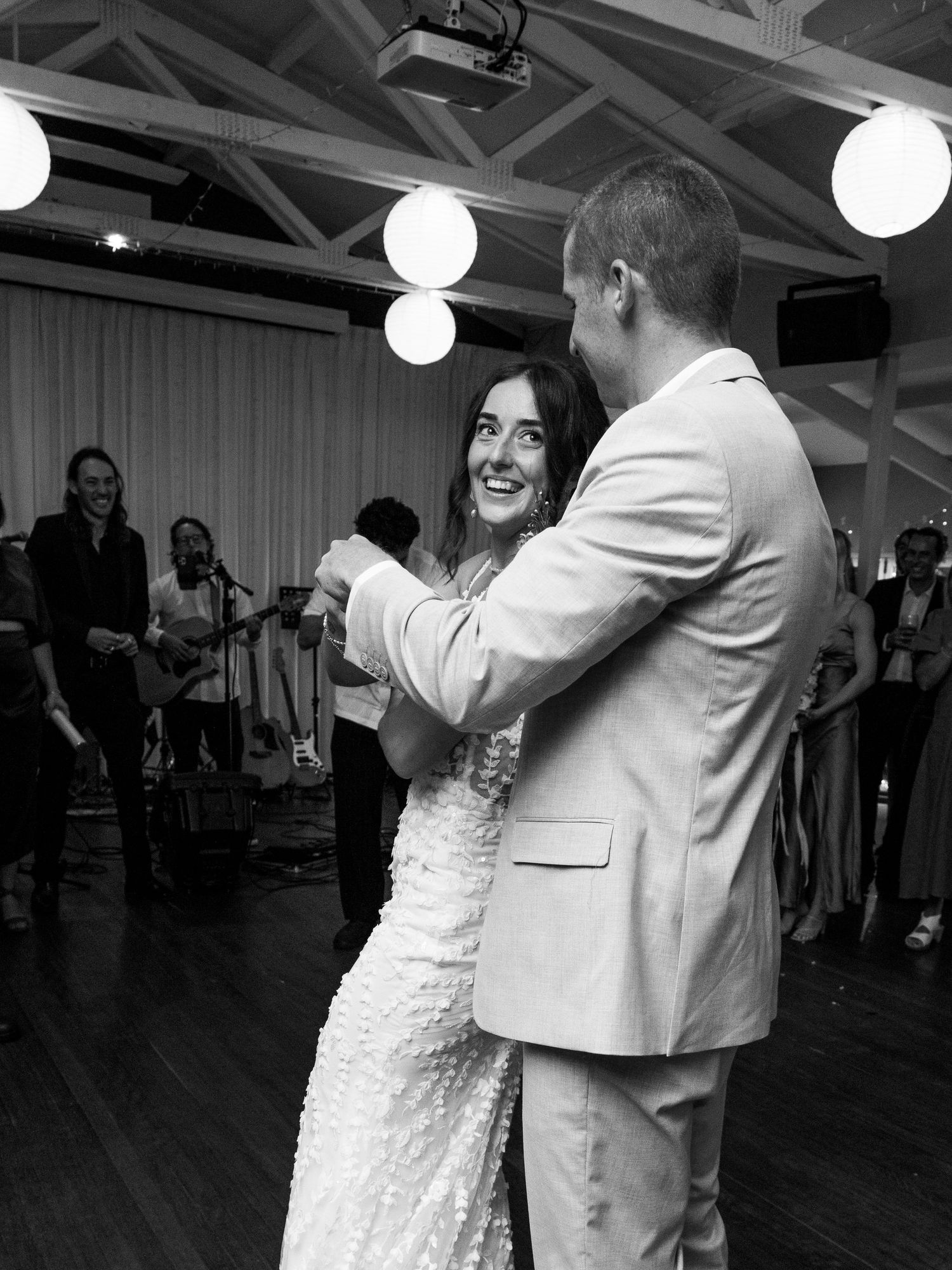 A couple in formal attire dances together at a wedding reception with glowing spherical lights in the rafters.