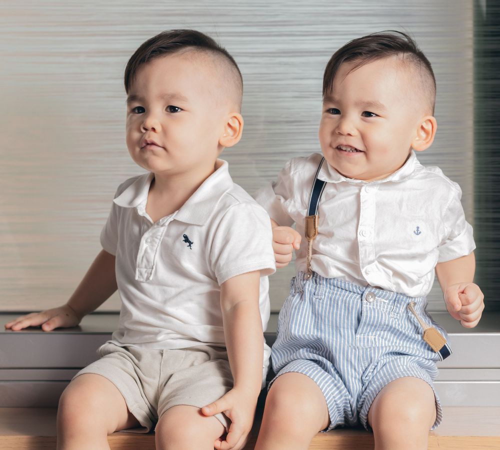 Two babies sitting together wearing white shirts and blue striped pants, shown in a series of candid poses.