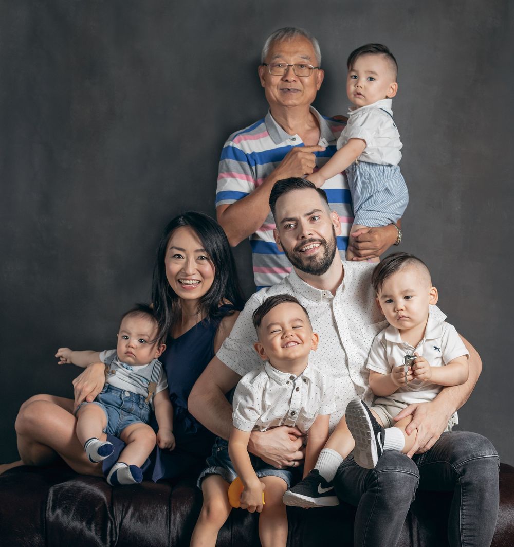 A family poses together against a dark studio backdrop for a professional portrait session.