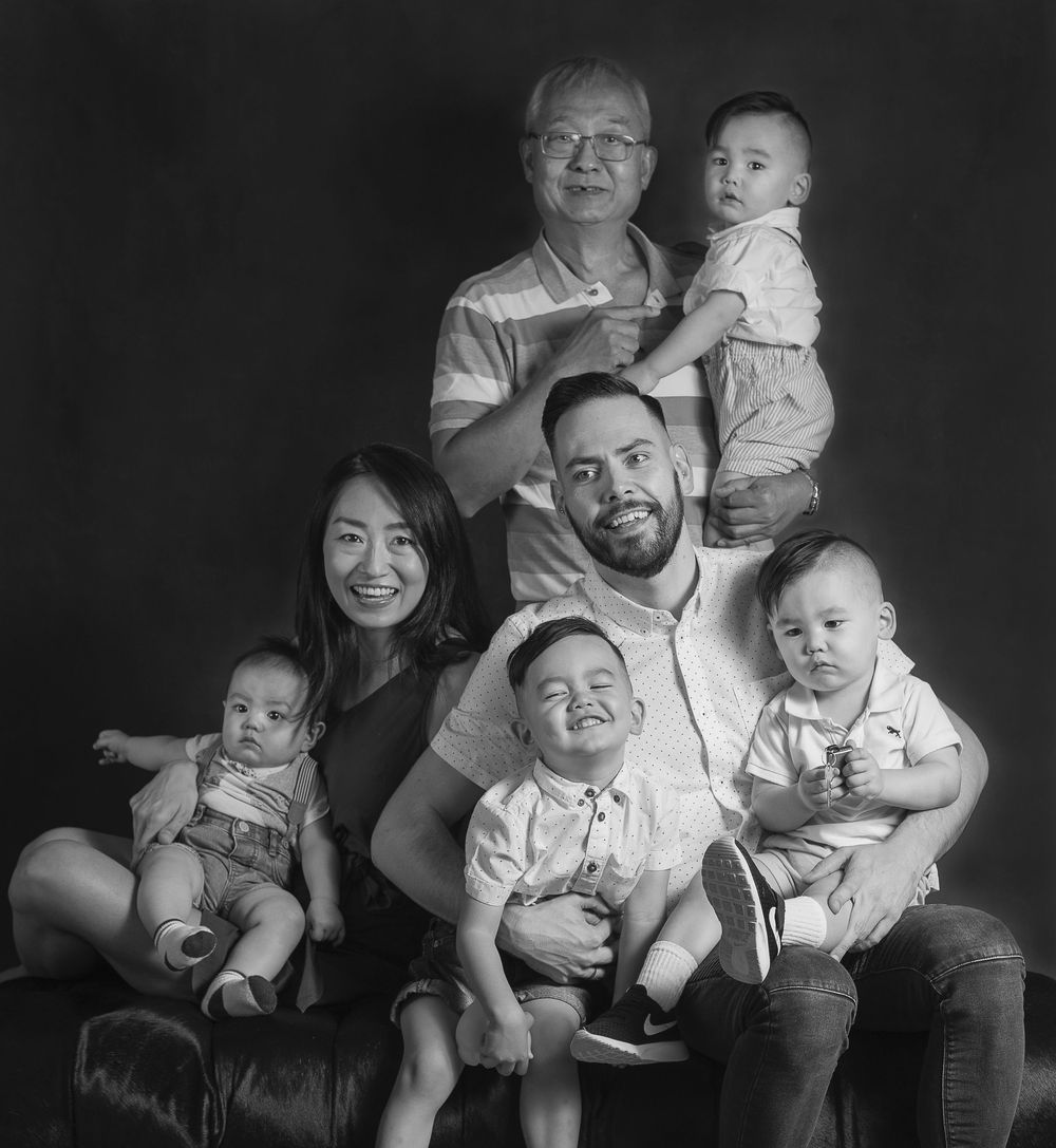 Black and white studio portrait of three generations of a family posed together in casual attire.