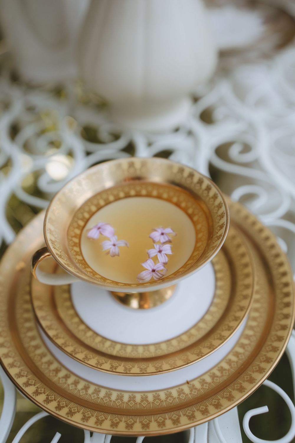 Elegant vintage teacup and saucer set in gold and white with delicate pink cherry blossoms on ornate lace tablecloth.