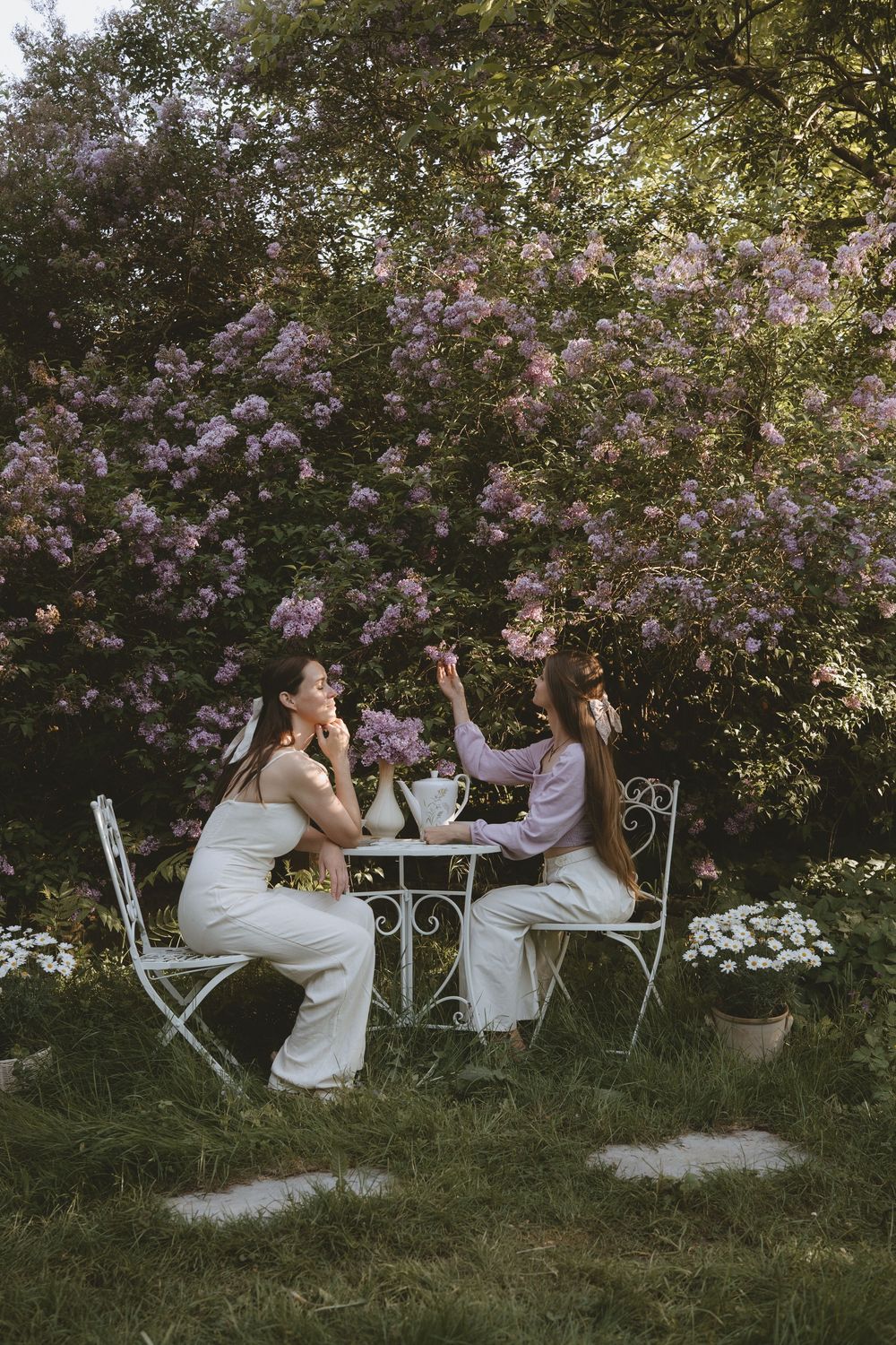 Two people enjoy afternoon tea at a vintage garden table beneath blooming pink cherry blossoms.