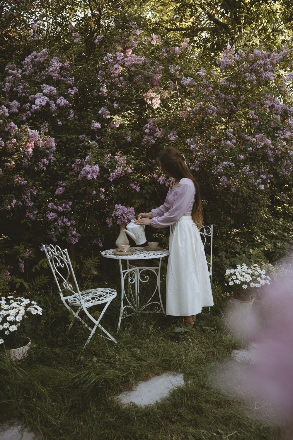 A romantic vintage garden tea setting with purple flowers and white furniture.