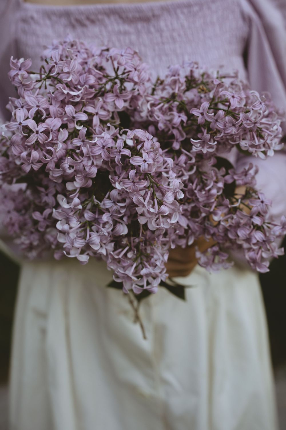A delicate bouquet of light purple lilac flowers held against a white fabric background.