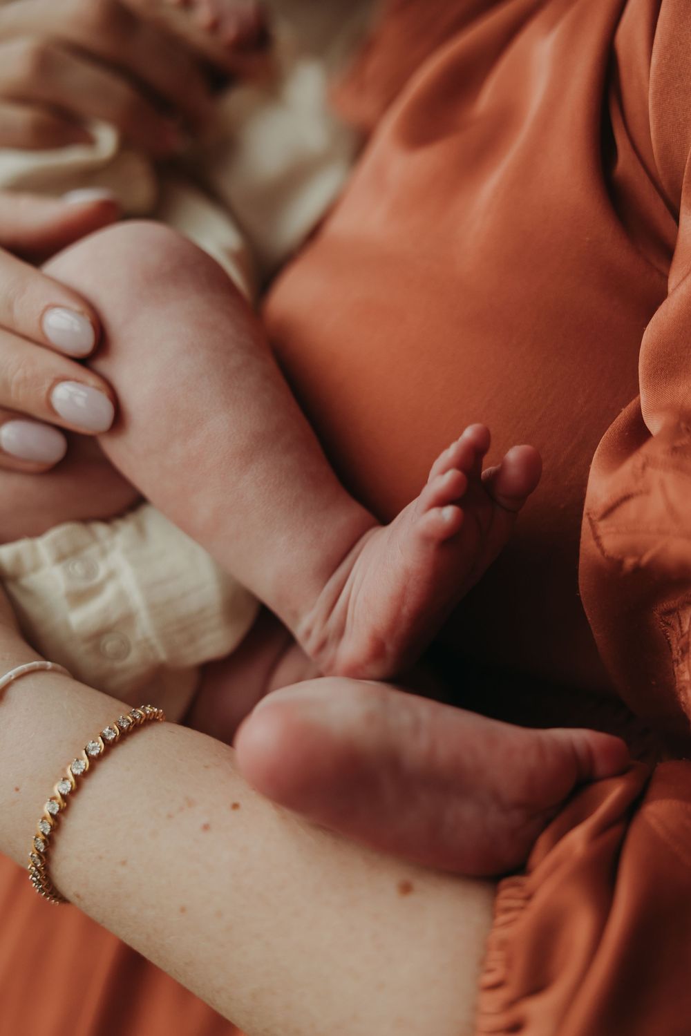 Close-up shots of a baby wearing gold jewelry while wrapped in a soft rust-colored blanket.