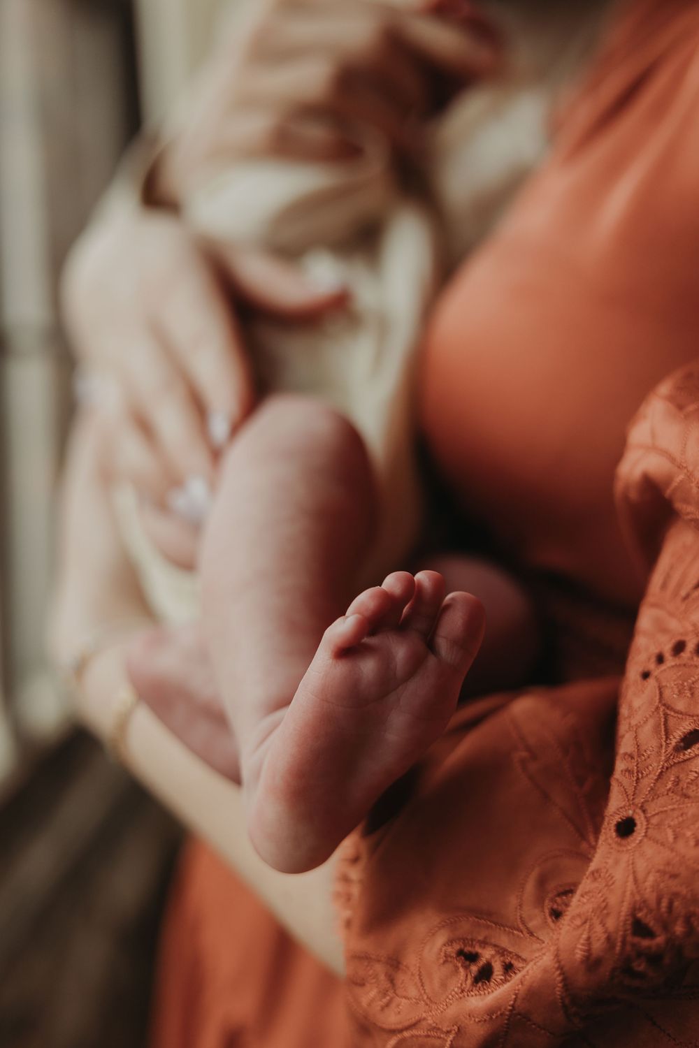 Close-up photograph of a tiny baby foot against an orange lace dress in soft, dreamy natural lighting.