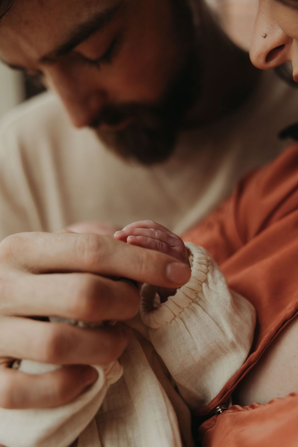 A tender moment between parent and infant as their hands touch in a warm, softly lit photograph.