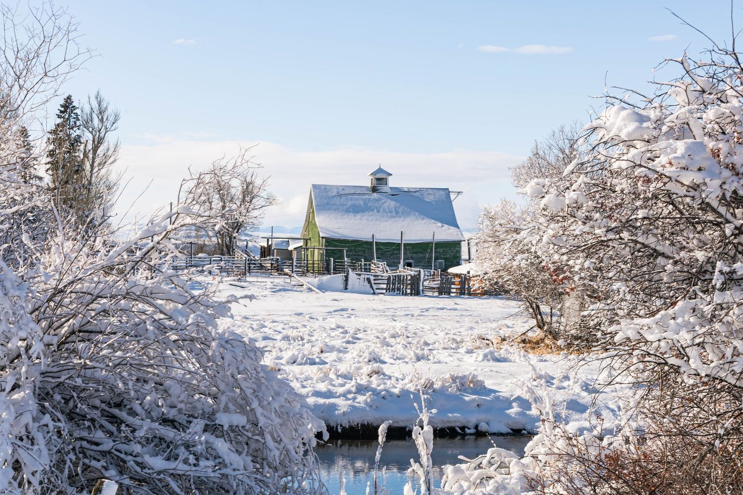 Panoramic view of a rustic farmhouse nestled in golden prairie fields with majestic mountains rising in the background.