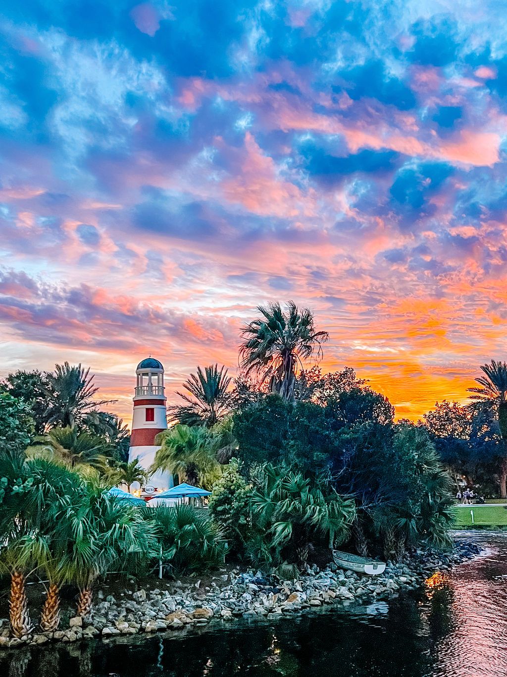 Stunning sunset view of a coastal resort with palm trees and white buildings against pink and orange sky.