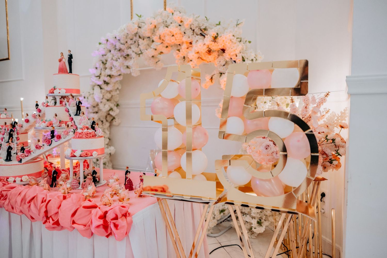 Decorative pink and white floral wedding reception arch and table setup with romantic lighting and decor elements.