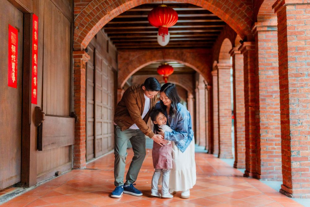 Red lanterns hang from a historic brick archway corridor with a family sharing an embrace under the covered passway.