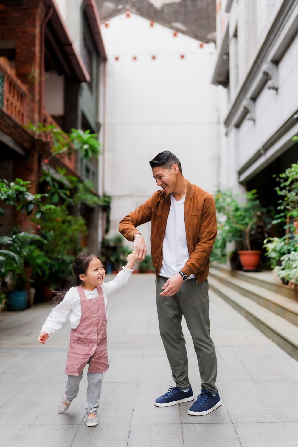 A playful sequence showing a small child in pink overalls with their father running and playing in an outdoor walkway.