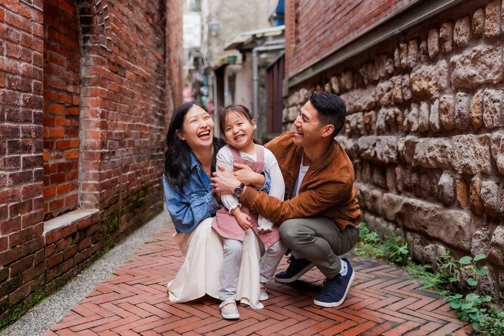 Candid moments of a family kneeling and laughing together against a rustic brick alleyway