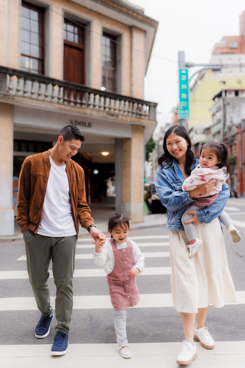 Family with two small children enjoying a fun moment together crossing on a city street wearing casual attire.