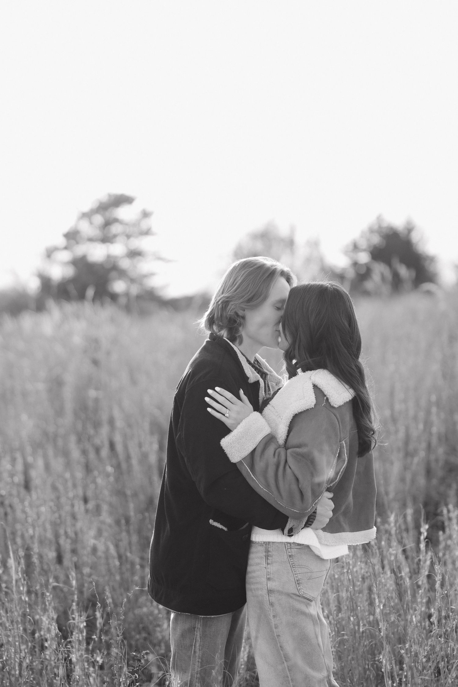 Romantic couple sharing intimate moments in a sunlit field of tall grass at sunset.