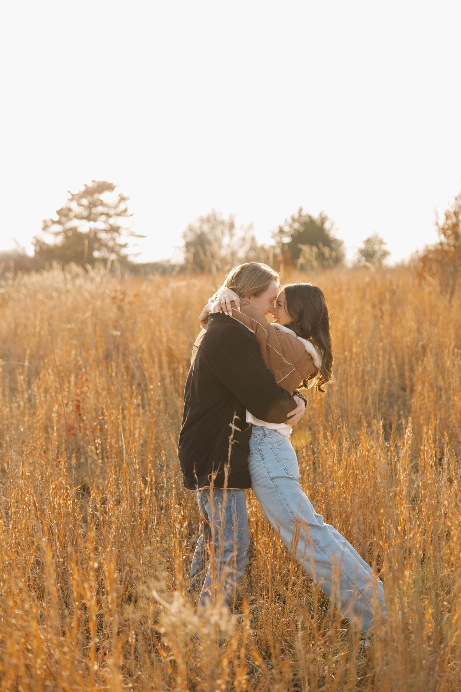 Two people share an intimate moment while standing in tall grass illuminated by warm sunlight.