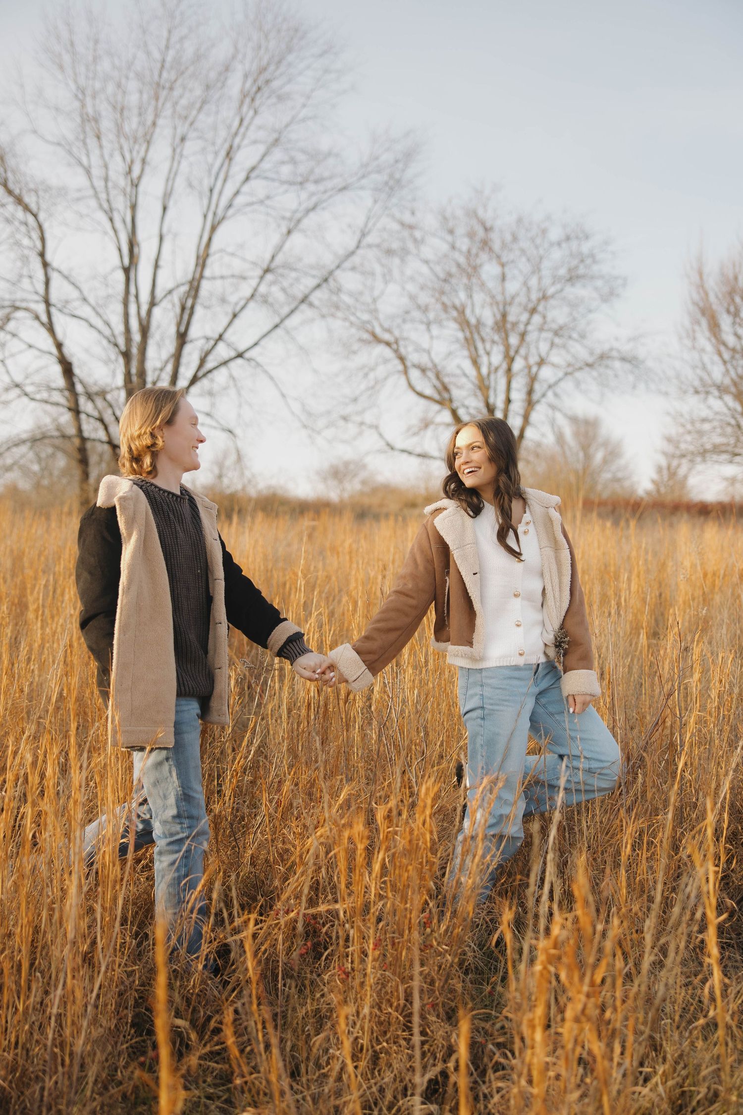 Couple walking and holding hands through golden prairie grass during autumn.