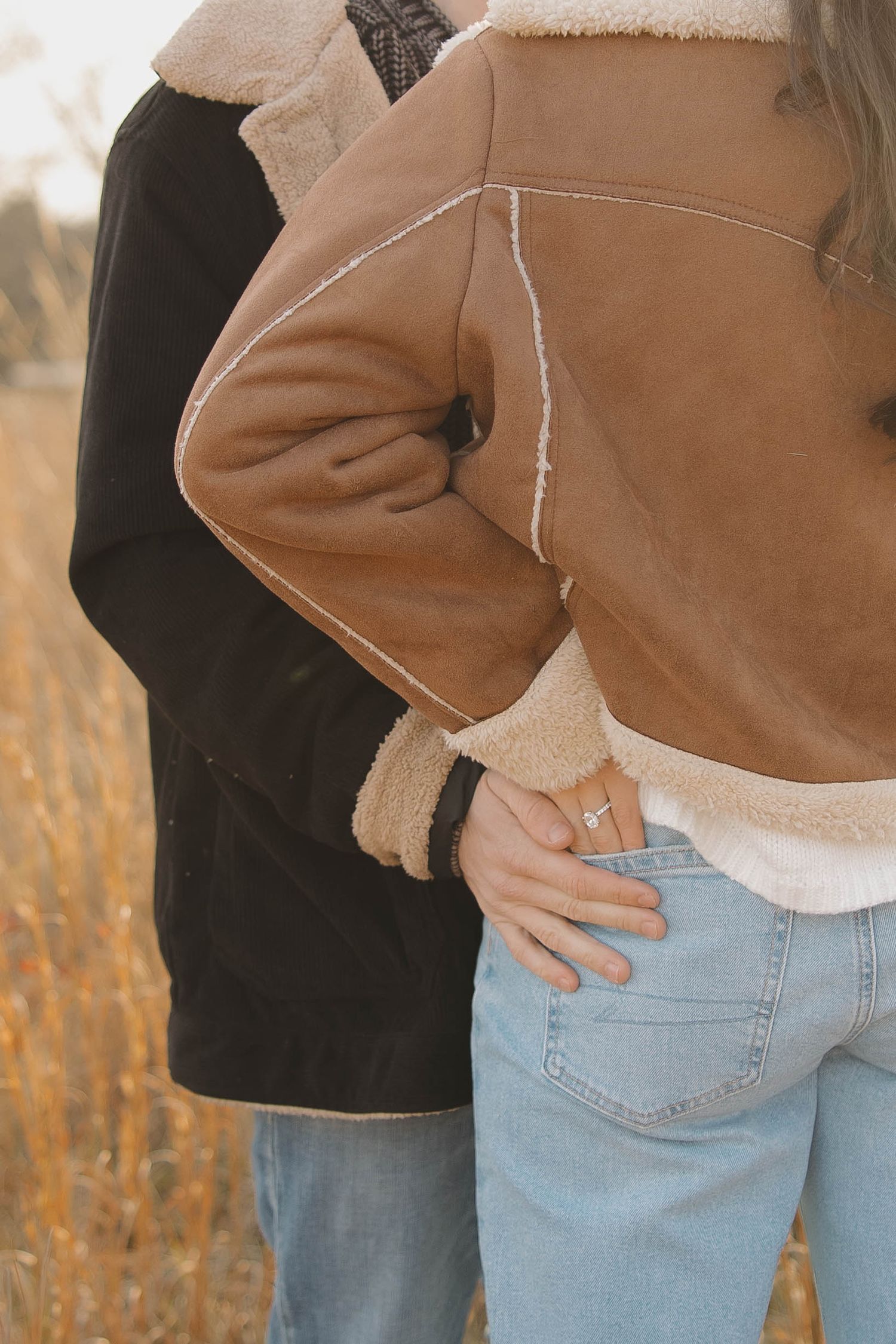 Close-up view of light blue denim jeans with back pockets and a beige sherpa jacket in warm autumn lighting.