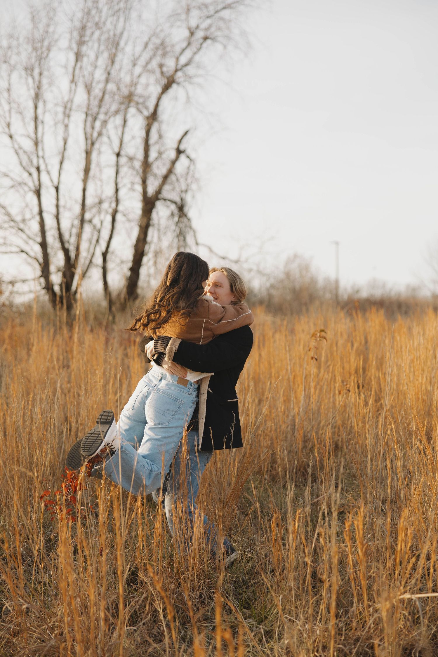 A romantic embrace captured in a golden field of tall grass during sunset.