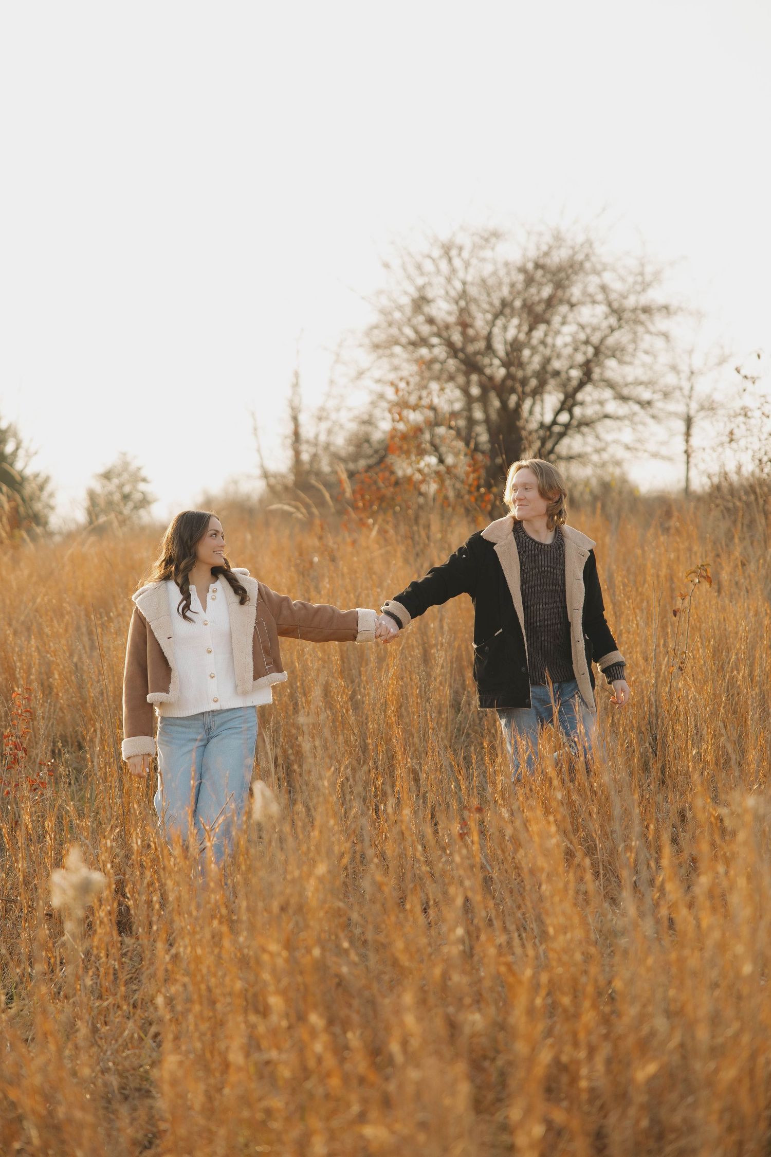 Two people walking together through a field of dried grass in warm evening light.