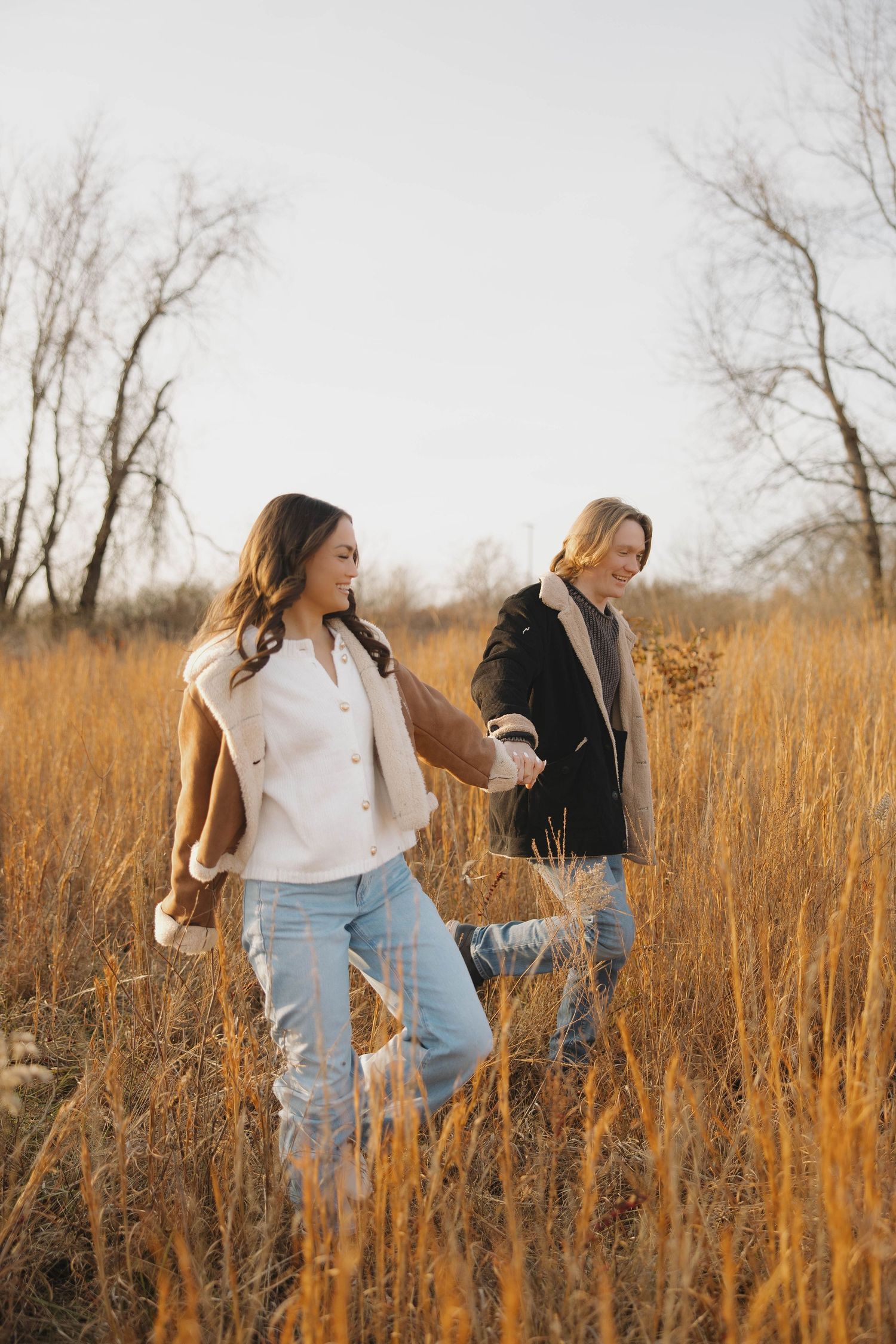 Friends laughing and dancing together in a sunlit autumn field.