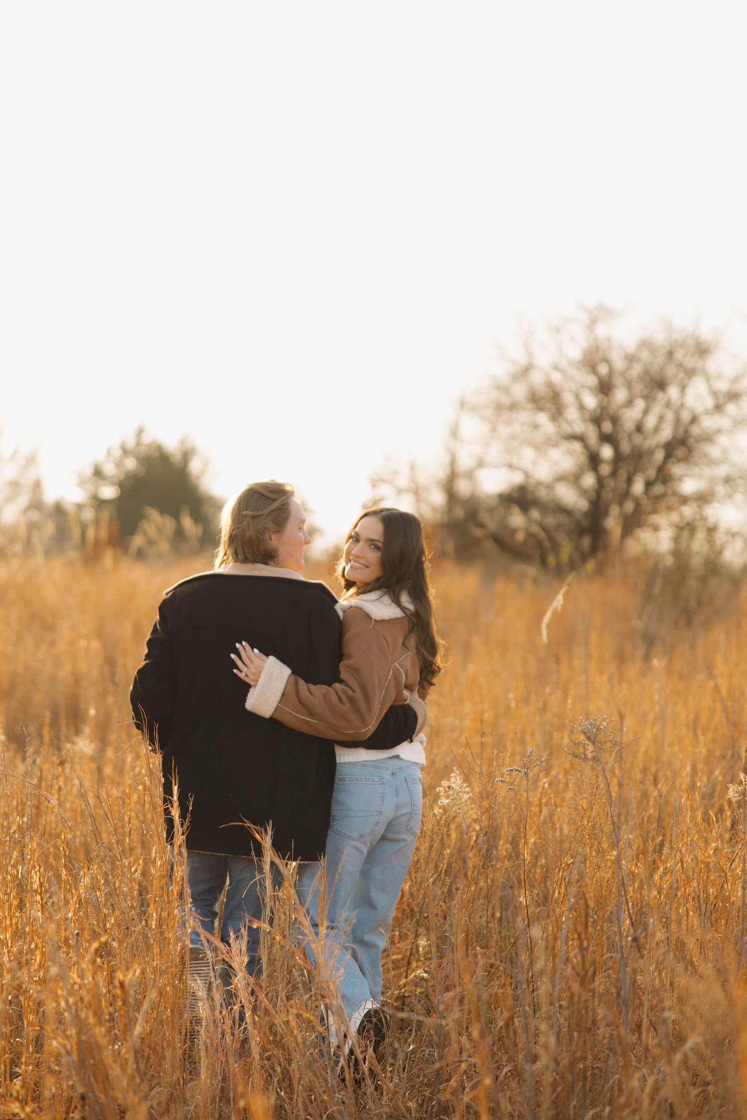 Two people embrace in a golden field of tall grass at sunset.