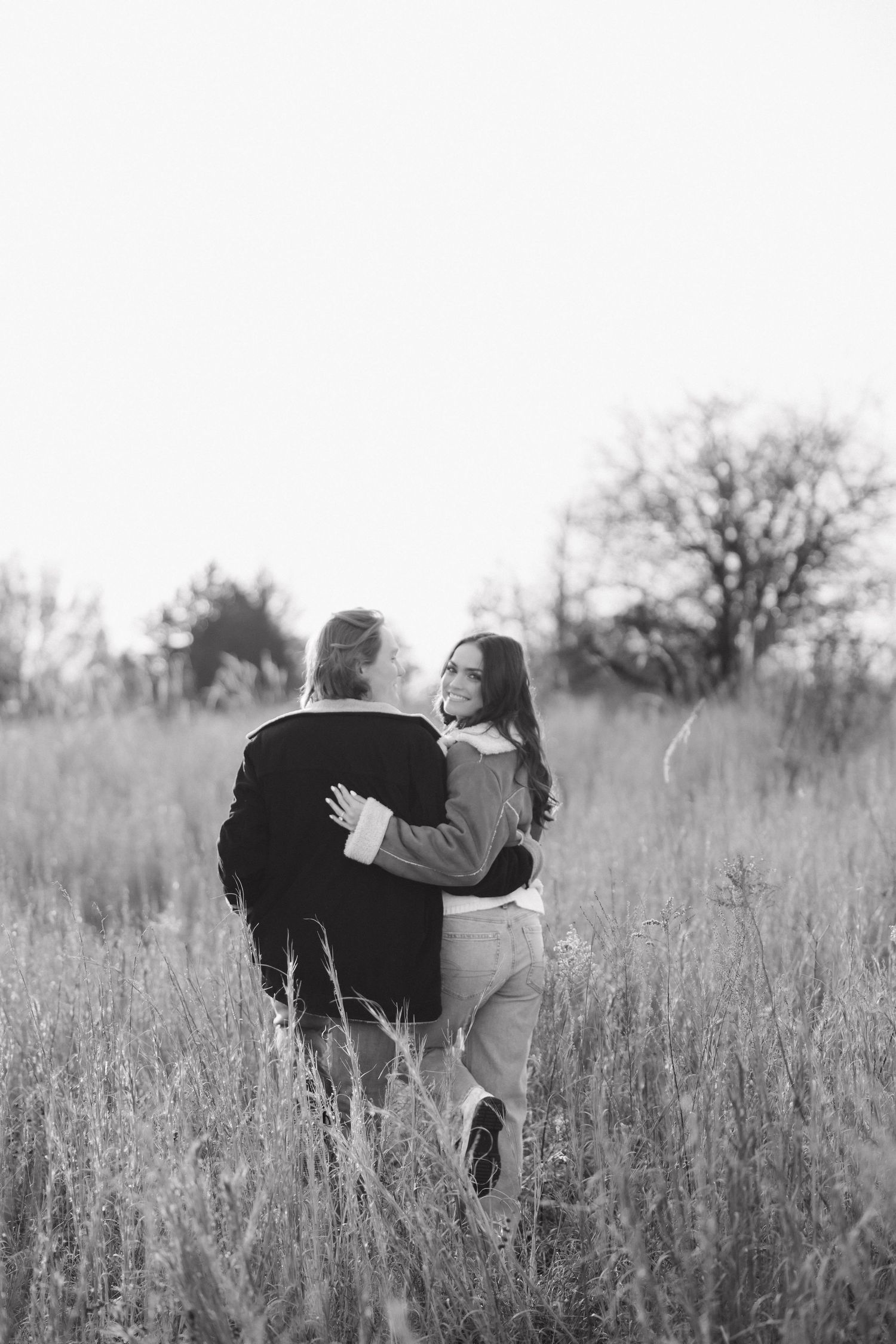 Black and white photo of a couple dancing together in a meadow of tall grass.