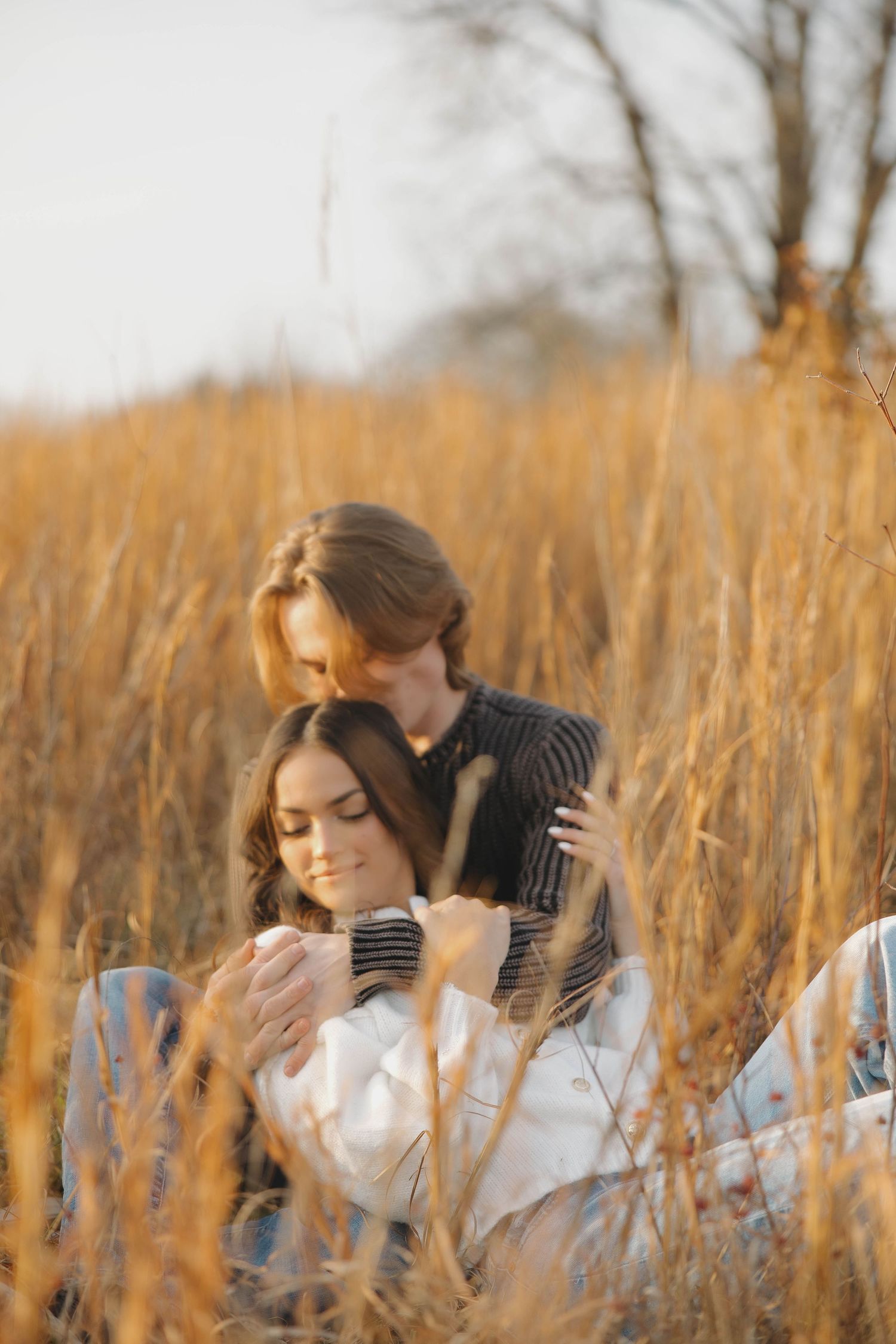 Two people laying down in autumn grass with soft golden sunlight filtering through.