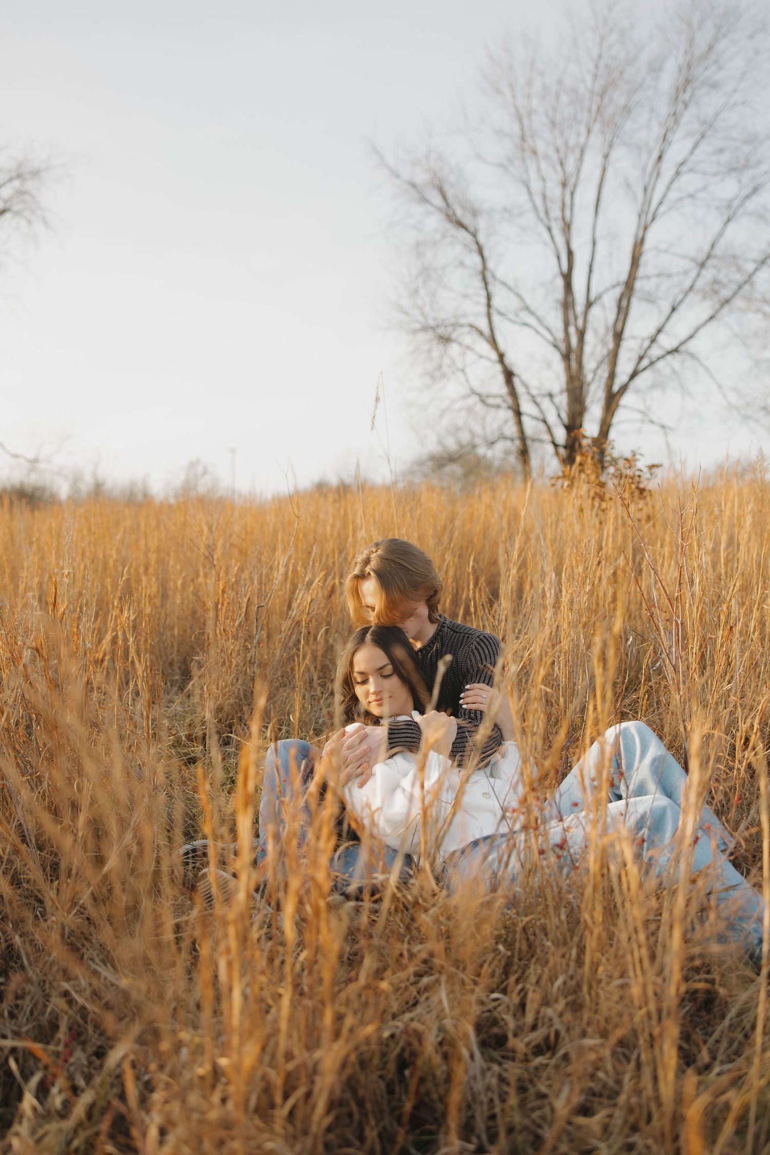 A family sits together in a field of tall golden grass during sunset creating a warm autumn scene.