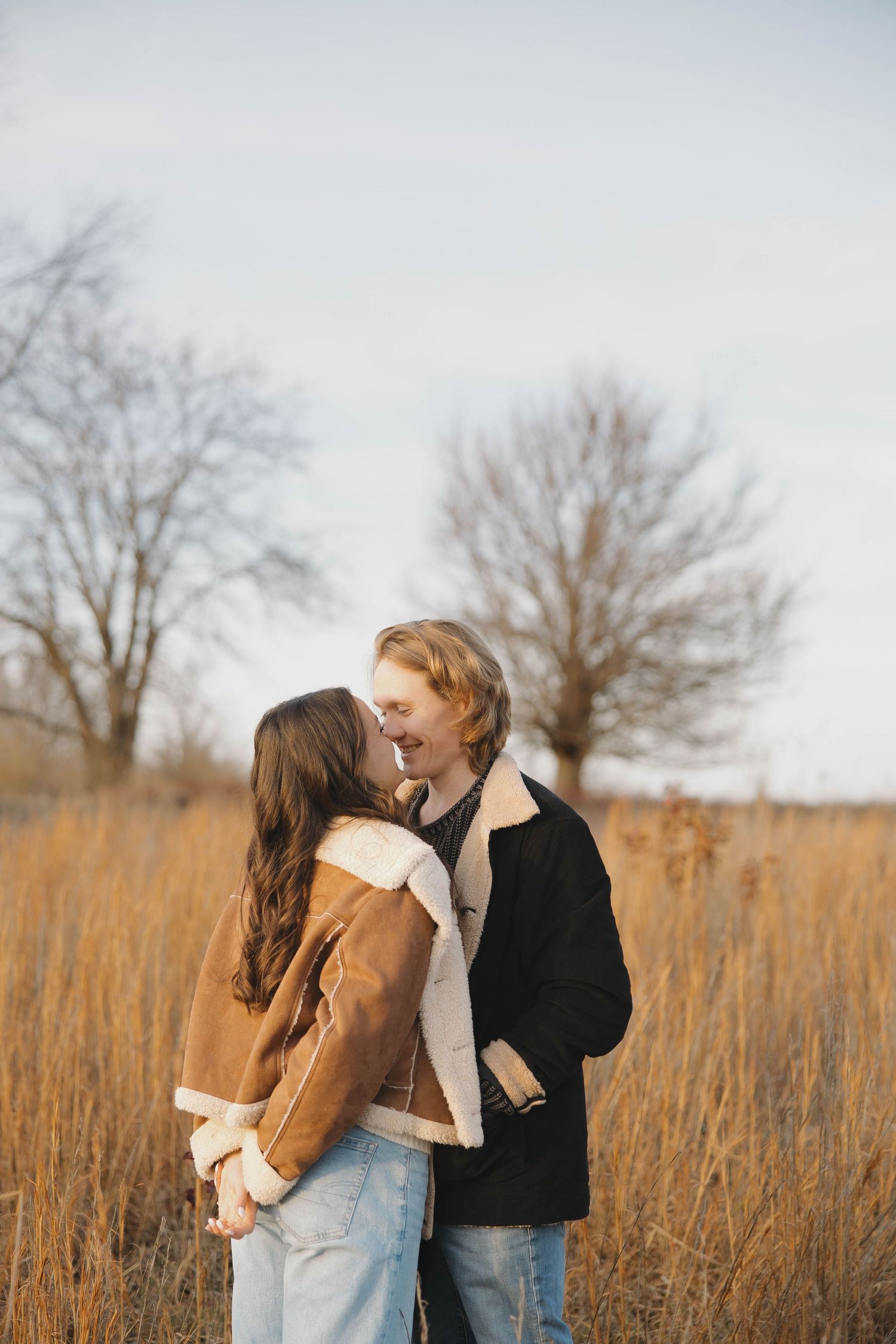 Couple sharing an intimate moment in a sun-drenched field of tall grass.