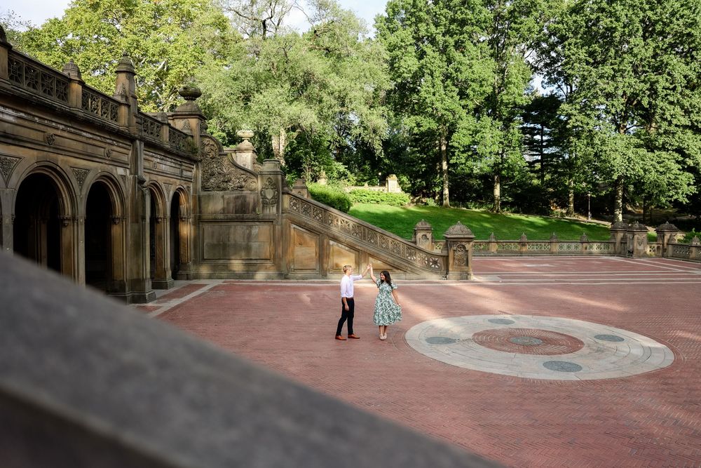 People walking along the winding brick paths and stone staircases of Central Park's Bethesda Terrace on a sunny day.