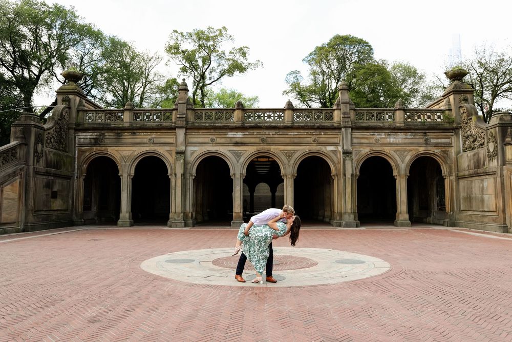 Historic stone terrace with ornate arched colonnade and brick paving surrounded by trees and landscaping.