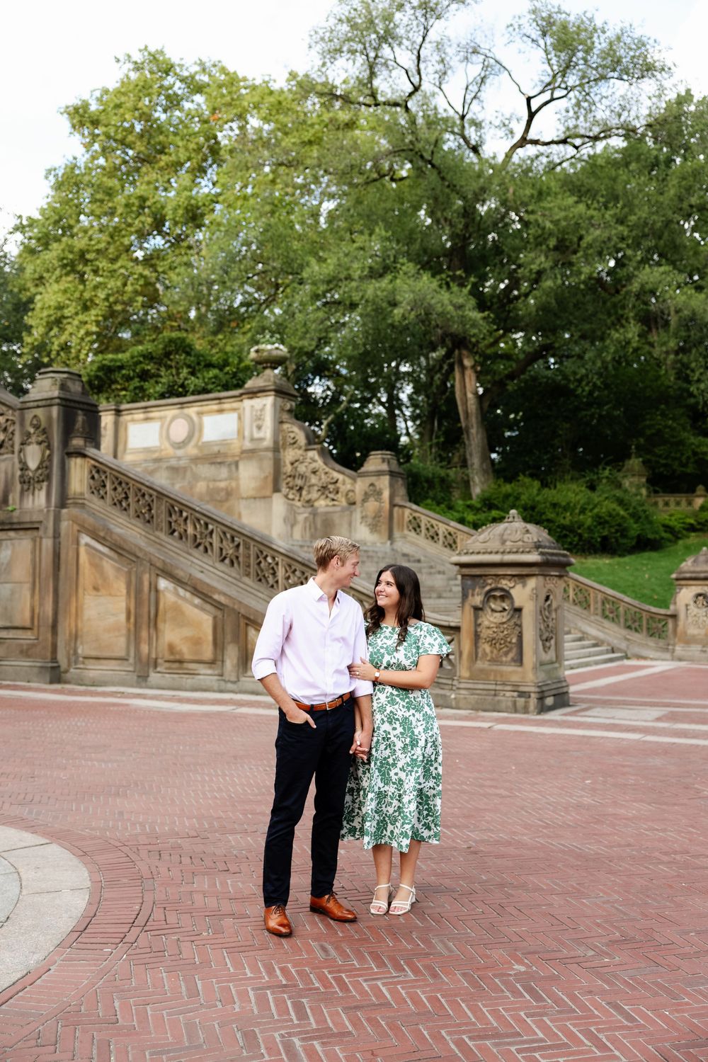 Two people share a tender moment on a historic brick terrace with decorative stone railings and steps.