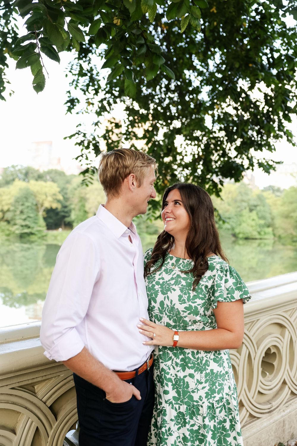 Couple sharing a romantic moment on a stone bridge surrounded by green trees in a park setting.